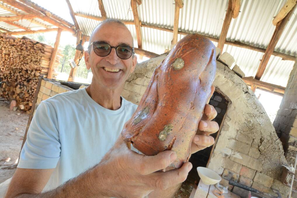 Beauty in imperfection: Steve Williams holds one of his vases that was fired in the hand-built woodfire kiln pictured behind him and includes a common feature of his work, the shell imprints of the setters. Photo: Scott Calvin.