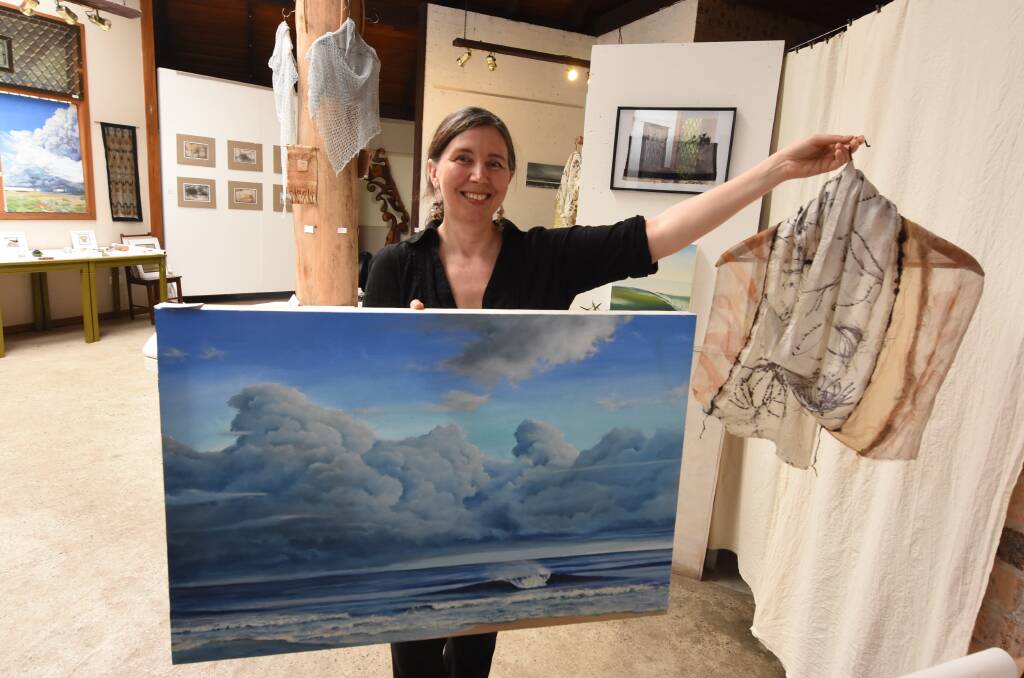 Summer holiday showcase: Jana Pearceova holds a painting by her husband Gerard and one of her textile works. Both are part of the exhibition currently showing at the Green Point Gallery. Photo: Scott Calvin.
