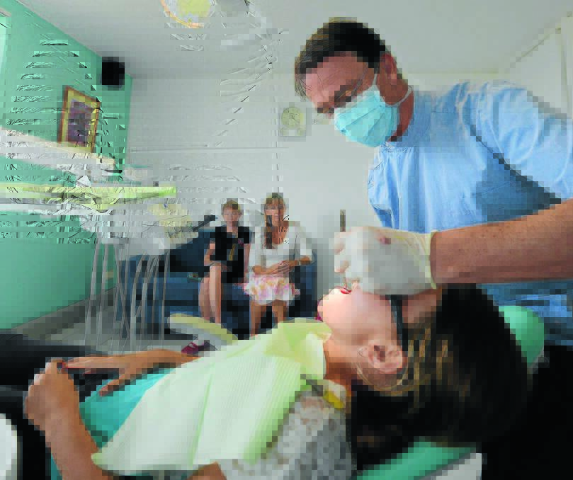 Isabelle Knaack delivers a wide smile to her dentist, Nick Mills at Albert Street Dental Practice. Her sister, Anneliese and mum, Julie, watch and wait for their turn to have their teeth checked for cavities.
