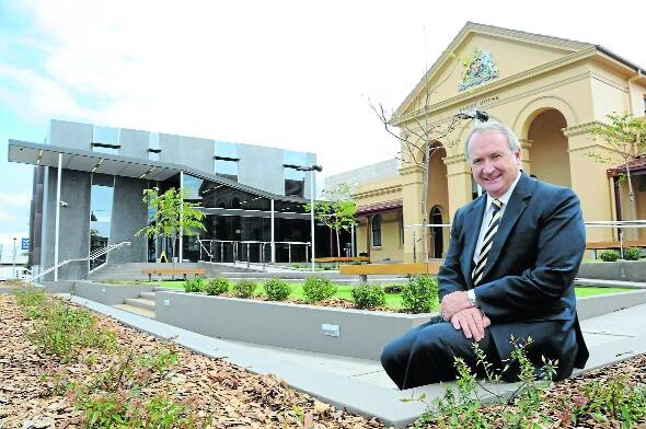 District Court judge and Local Court Chief Magistrate Graeme Henson seated in front of the new Taree Courthouse yesterday, with the 130-year-old courthouse to the right.