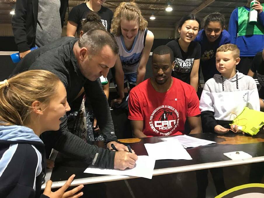 Sign here: Taree Basketball's Steve Atkins seals the deal with new player-coach Lonnie Funderburke, watched by Taree junior representative basketballers.