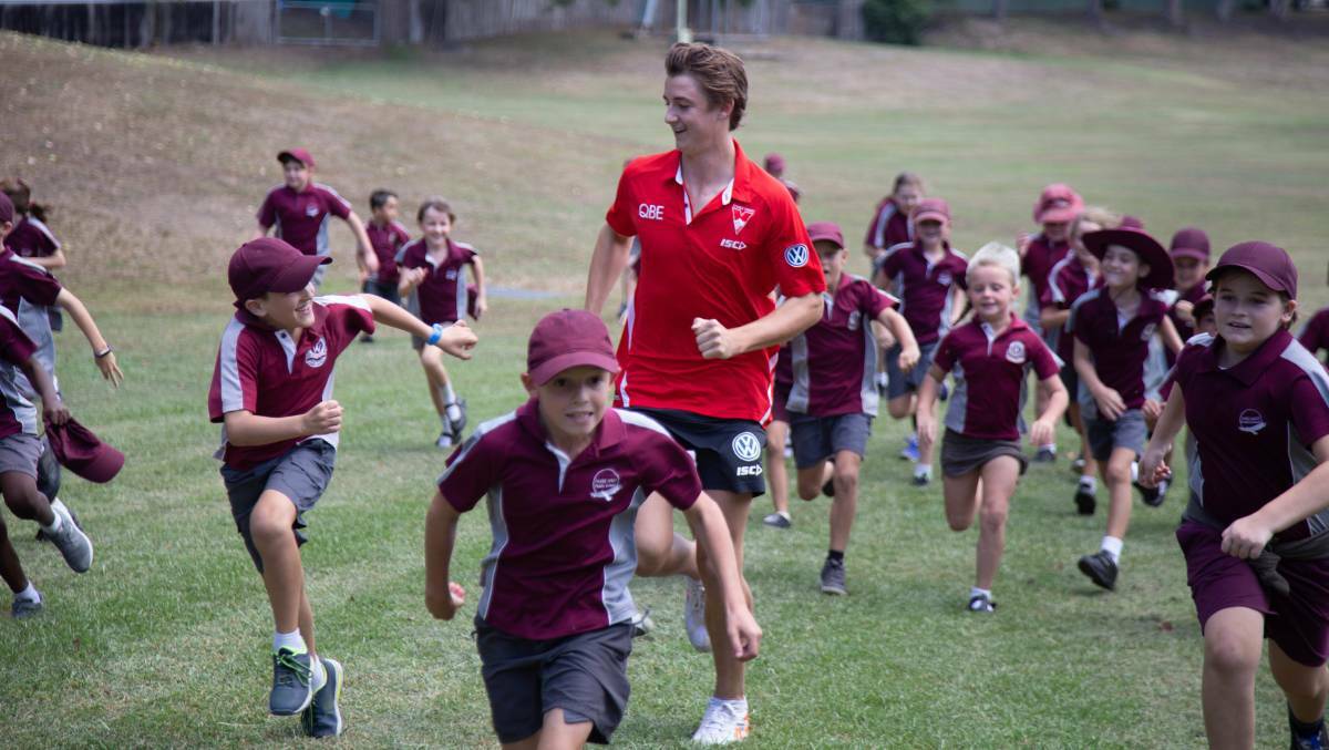 Swans player Harry Reynolds with Taree West Public School students during the team's visit to the region in 2019.