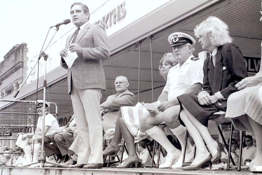 Greater Taree City mayor Les Brown speaking at the opening of the Manning Aquatic Festival in 1985. Ted Hill, the MC for the aquatic parade, is seated between Liz Hayes and Wendy Machin.