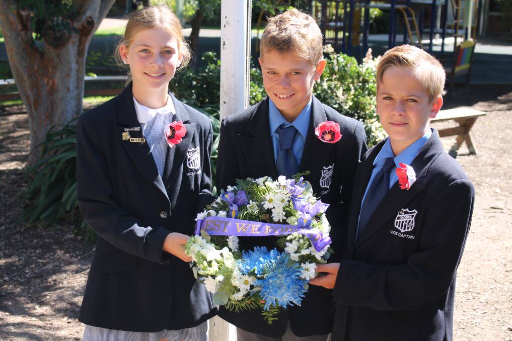 Respect: Tinonee Public School captain Isaac Martin (centre) and vice captains Jorja Holborow and Sam Burke with the Anzac commemorative wreath which was placed at the flagpole during the Anzac service at the school.