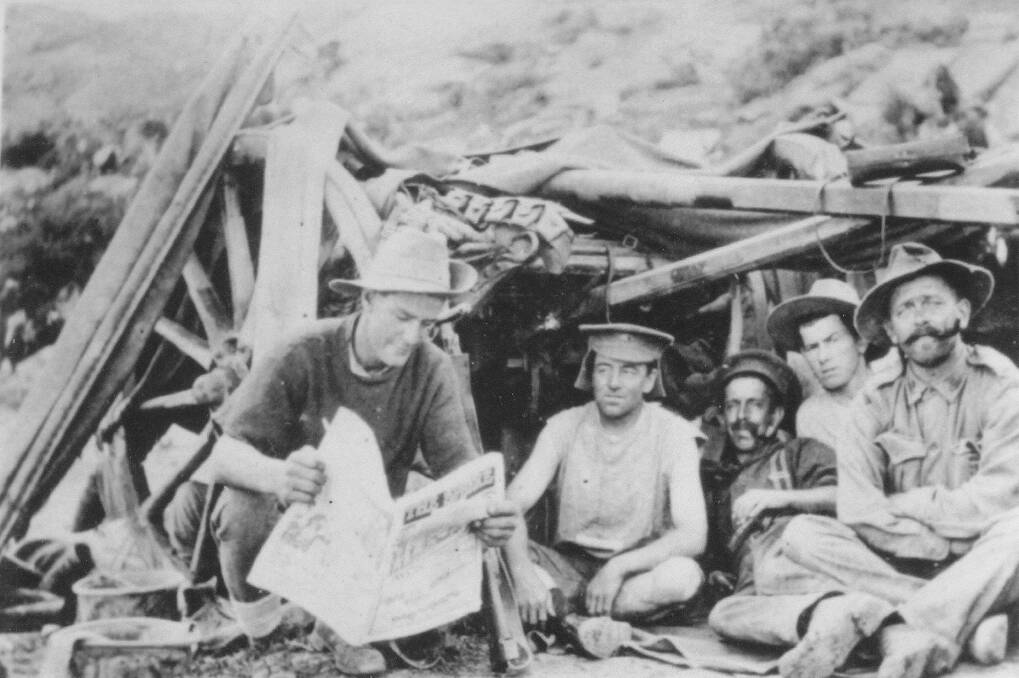Edward Bourke (left) reads a newspaper in a trench with other diggers at Gallipoli. The photo was taken by a war correspondent.