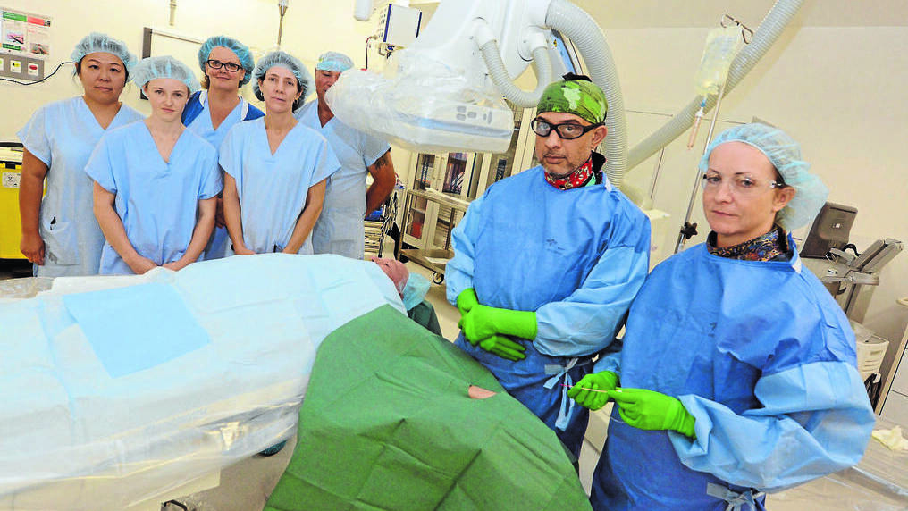 Cause to swear: Cardiologist Dr Sesh Narasimhan stands ready to do a cardiac procedure in the Mayo Private Hospital Cardiac Catheter Laboratory. Dr Narasimhan and his team Linda Pearce, Cindy Bradshaw, Alyce Inman, Max Minnett, Toni Vause and scrub nurse (right) Rhian Lewis seek public patient access to the private hospitals cath lab facilities.