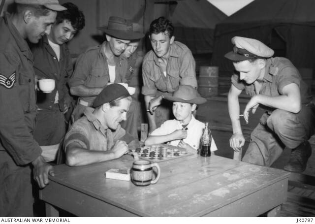 Kimpo, South Korea in 1953. Korean youngster Jimmy plays draughts with Leading Aircraftman Lance Lee of No. 77 Squadron, RAAF. No. 77 Squadron headquartered at RAAF Base Williamtown. Photo: the Australian War Memorial JK0797