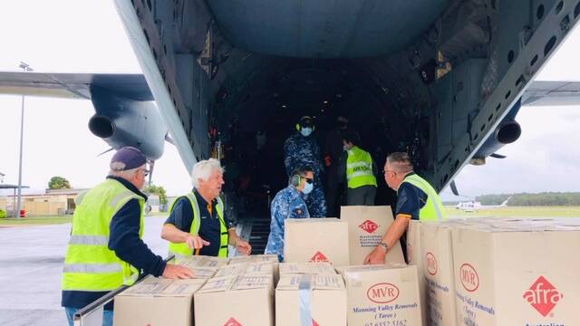 The Rotarians and RAAF crew load the boxes on to the aircraft.